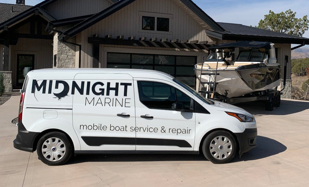 White van with 'Midnight Marine' branding parked in front of a house with a boat.
